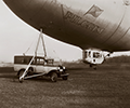 Goodyear's Pilgrim, built in 1925, was the first commercial non-rigid airship flown using helium. With a landing wheel replacing bumper bags and the first passenger car held flush against its bag by internal cables, Pilgrim's contributions to aeronautics were recognized by the Smithsonian Institution, which exhibited the airship as a milestone in aviation progress. The mast, called a belly mooring, was an experimental portable design developed in 1930 to enable cross-country operations independent of permanent hangars.
